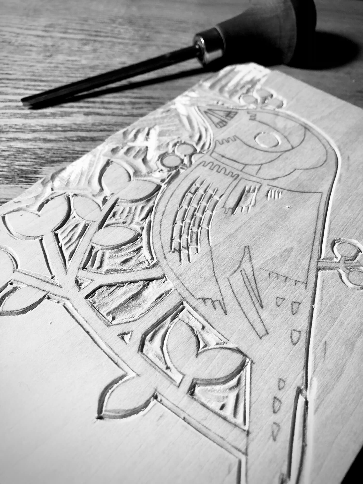 Wooden block with carved design and a carving tool on a wooden surface