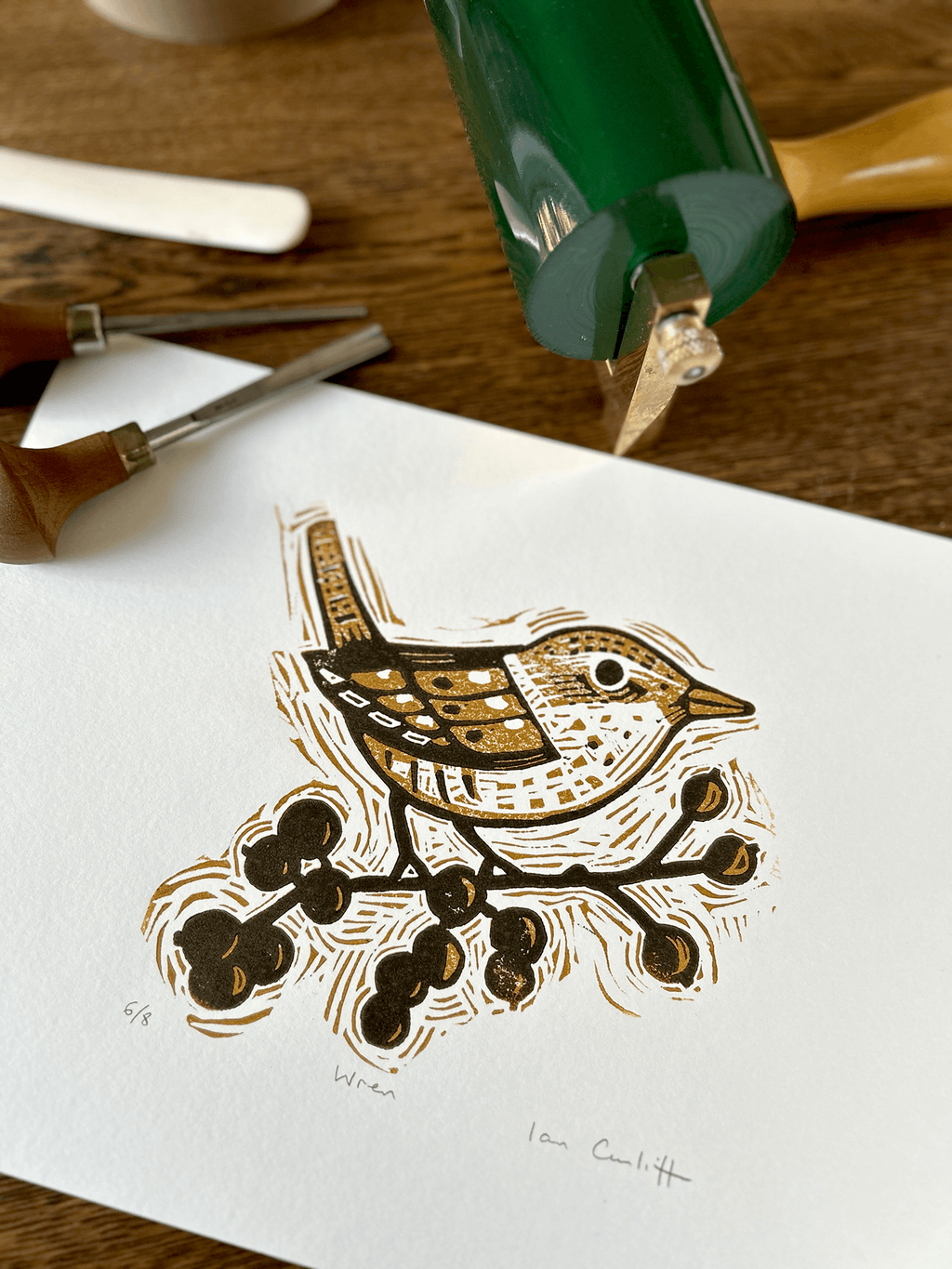Woodcut print of a bird and berries on white paper with carving tools in the background.