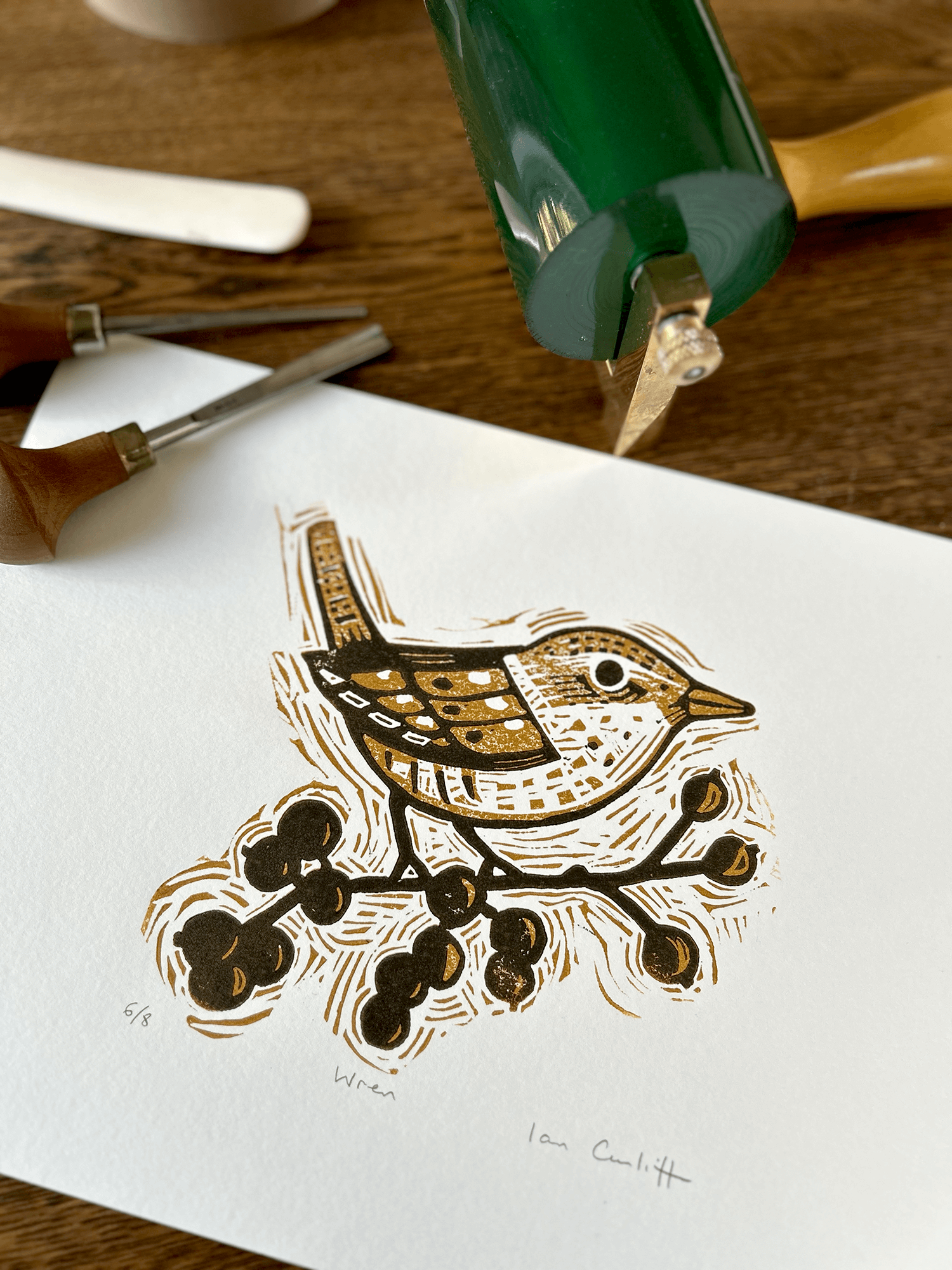 Woodcut print of a bird and berries on white paper with carving tools in the background.