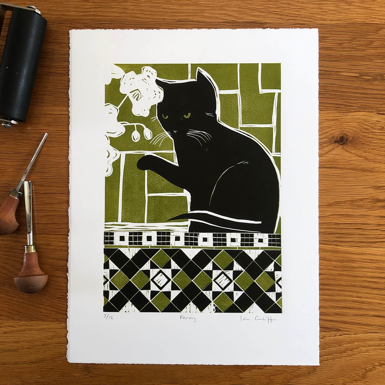Print of a black cat with green patterns on a wooden surface with printmaking tools.