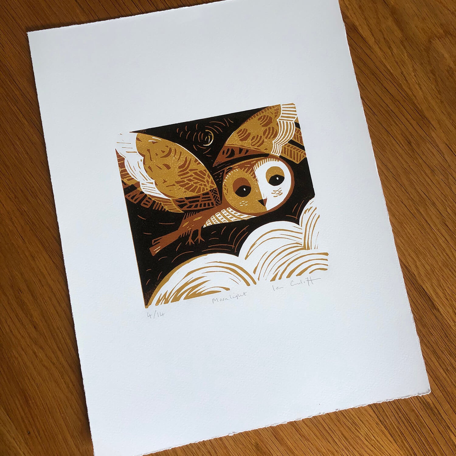 Illustration of an owl on a white card with gold accents, placed on a wooden surface.