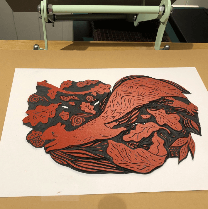 Woodcut-style illustration of a squirrel on a white sheet of paper with a printing press in the background.
